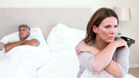 una pareja molesta sentada en una cama.