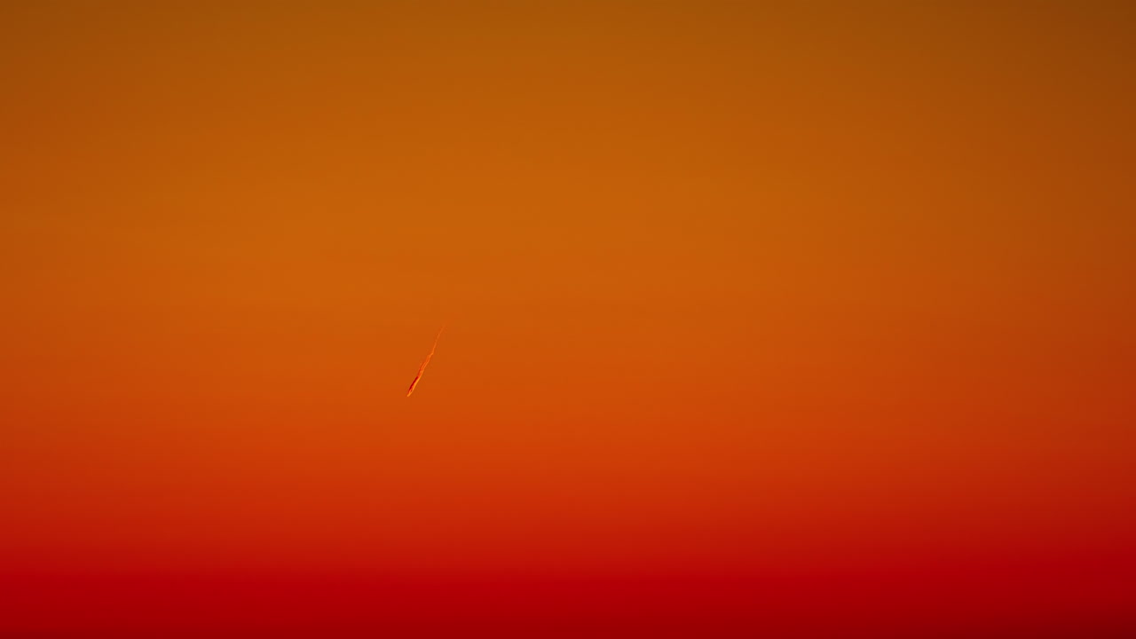 tomada de ángulo bajo de un avión dejando un rastro blanco antes de un cielo naranja profundo, imágenes de lapso de tiempo