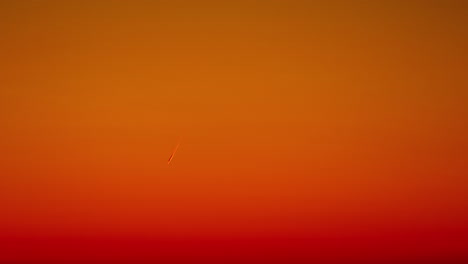 low angle shot of airplane leaving white trail before deep orange sky, timelapse footage