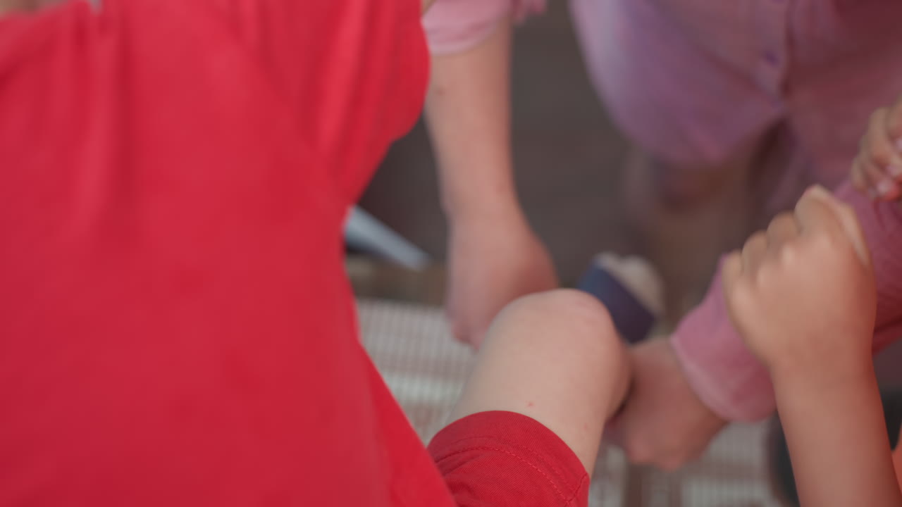 Parent Kneeling Putting Sock On ChildS Foot, Hands Adjusting Fabric And Toe, Morning Dressing Routine On Porch, Supportive Assistance And Gentle Focus, Small Foot Secured For Playtime
