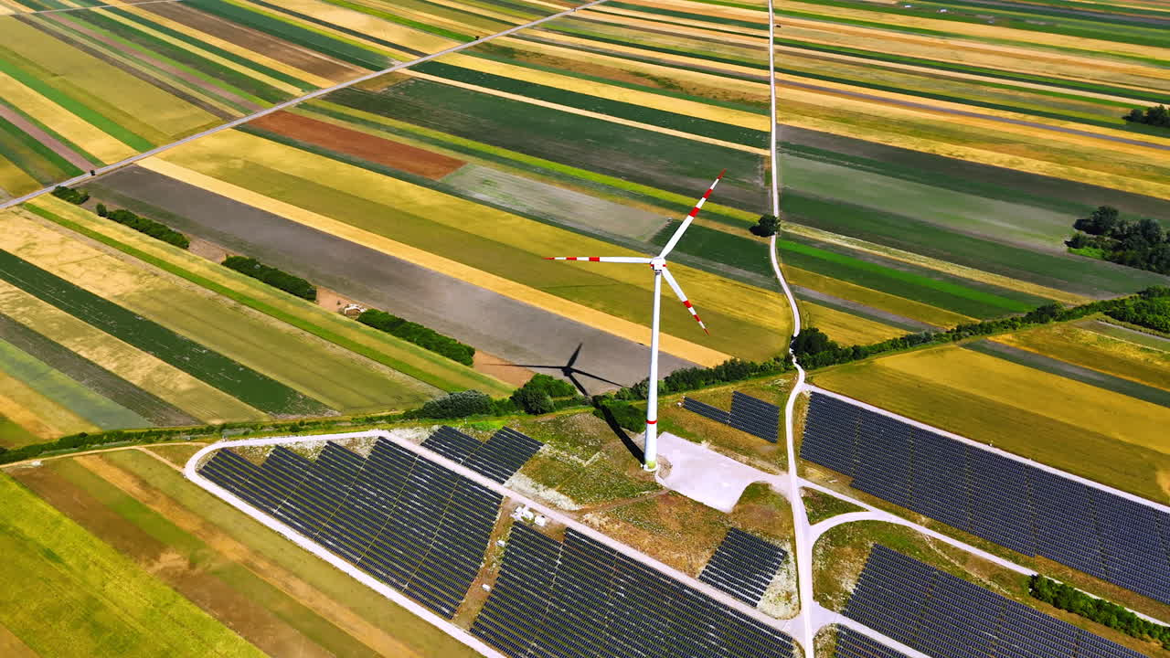 Striped colorful fields in the rural area. Drone footage over the solar panels site and rotating wins turbine