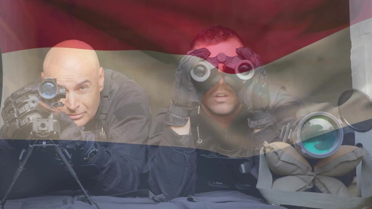 To soldater ligger ned, skarpskytte sigter, observatør løfter kikkert, scanner mål, flag vajer.