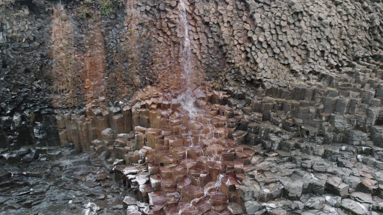 tiro de camiones de cascada que fluye por columnas de basalto cañón studlagil, islandia