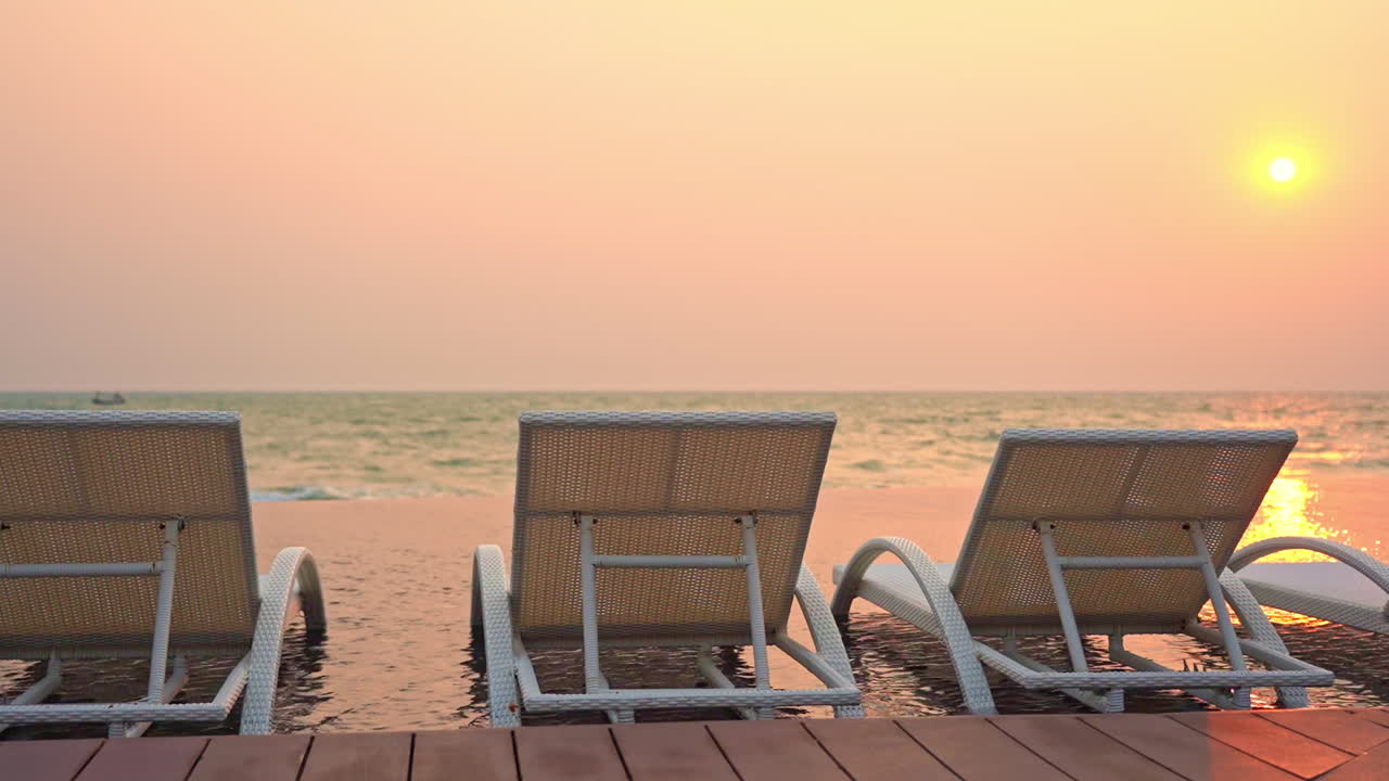 Static shot of beach sunbed loungers on the beach on the edge of an infinity pool during sunset