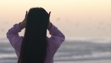 해가 질 때 갈매기가 배경으로 날아가는 동안 해변에서 머리를 손가락으로 달리는 소녀의 중간 샷
