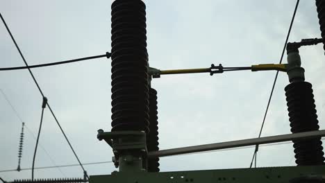 Electrical-insulators-and-connections-at-a-power-station,-cloudy-sky-backdrop