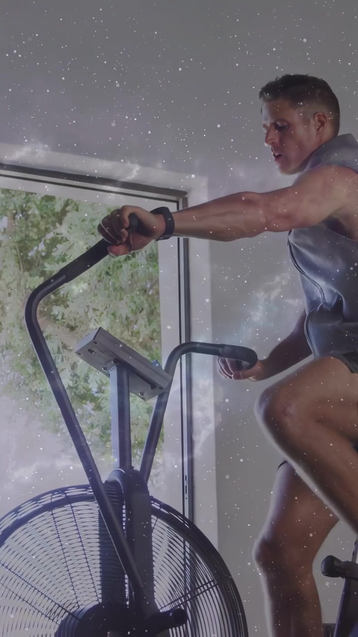 Vertical video: Man mounting air bike and pedaling, raising intensity for fitness with star overlay