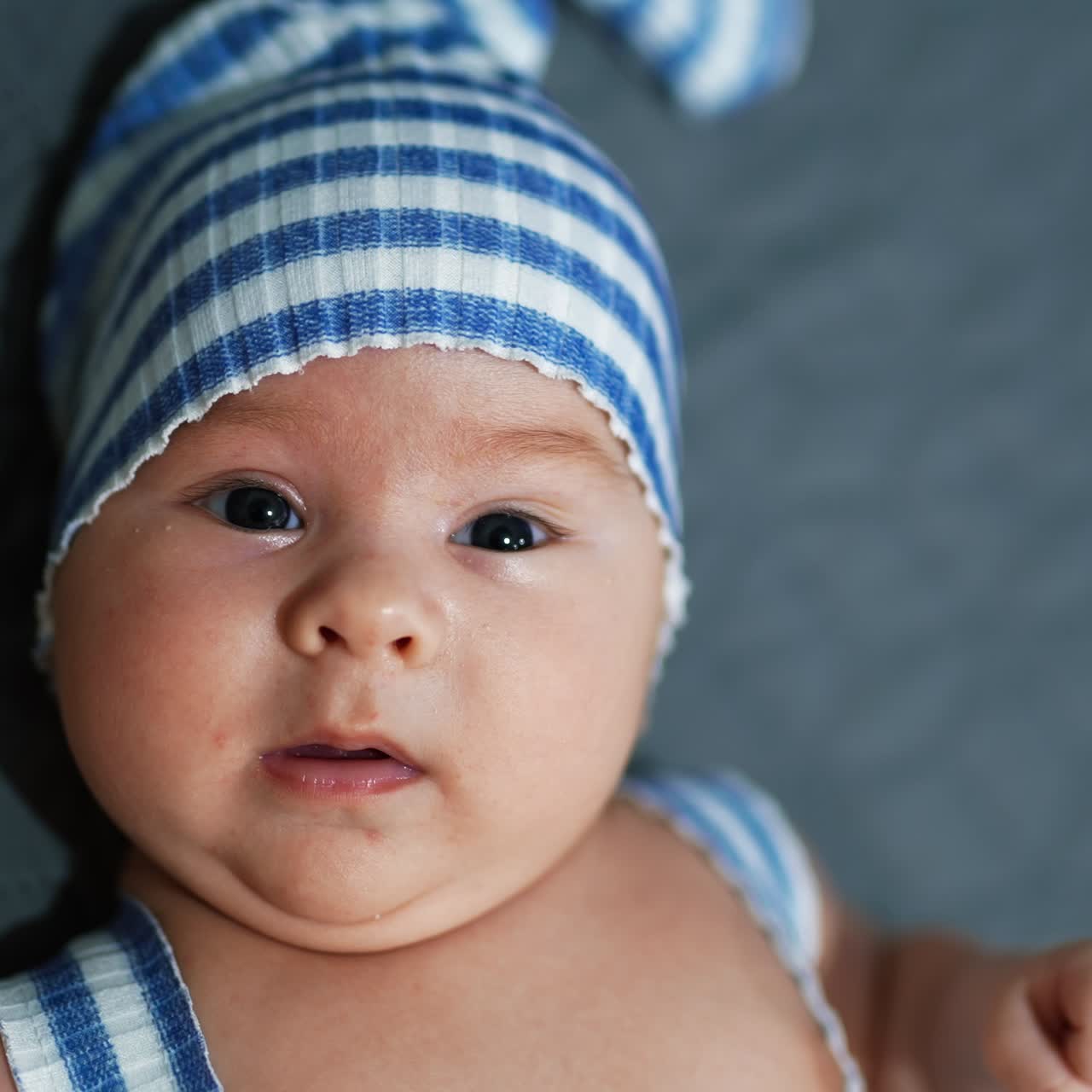 Cute toddler in adorable blue hat. Baby boy with plump cheeks at the grey backdrop. Face close up