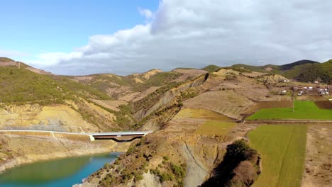 Aerial-view-of-rural-colorful-landscape-with-hills-and-planted-parcels-on-slope,-bridge-over-quiet-river