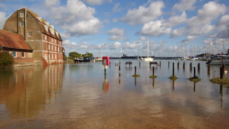 Panning-shot-of-watermill-with-benches-and-pathway-flooded-at-high-tide-at-Ashlett-creek-in-the-Solent,-Southampton