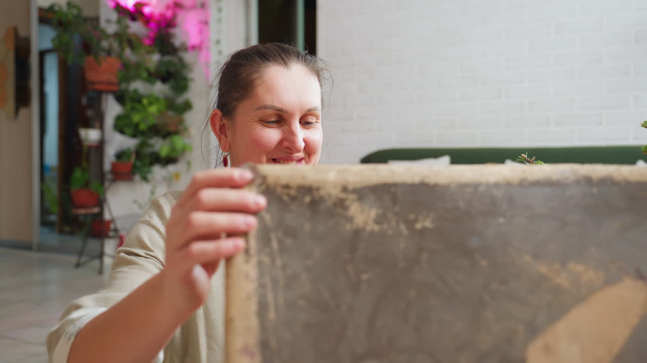 Woman opening old box with excitement, feeling overwhelmed with joy and happiness after discovering hidden treasures inside cozy living room decorated with green sofa, festive lights