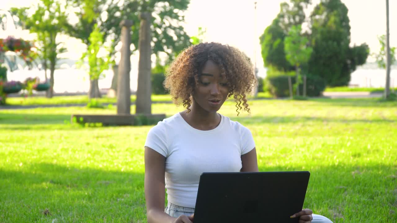 estudiante afroamericano e aprendiendo usando chat por webcam de computadora. mujer joven llamando en la computadora portátil habla con el profesor en línea estudiando en el parque de la universidad