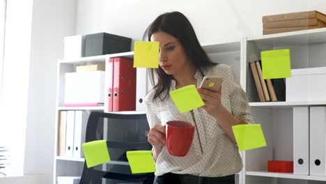 businesswoman standing near glass wall with sticky notes and using smartphone