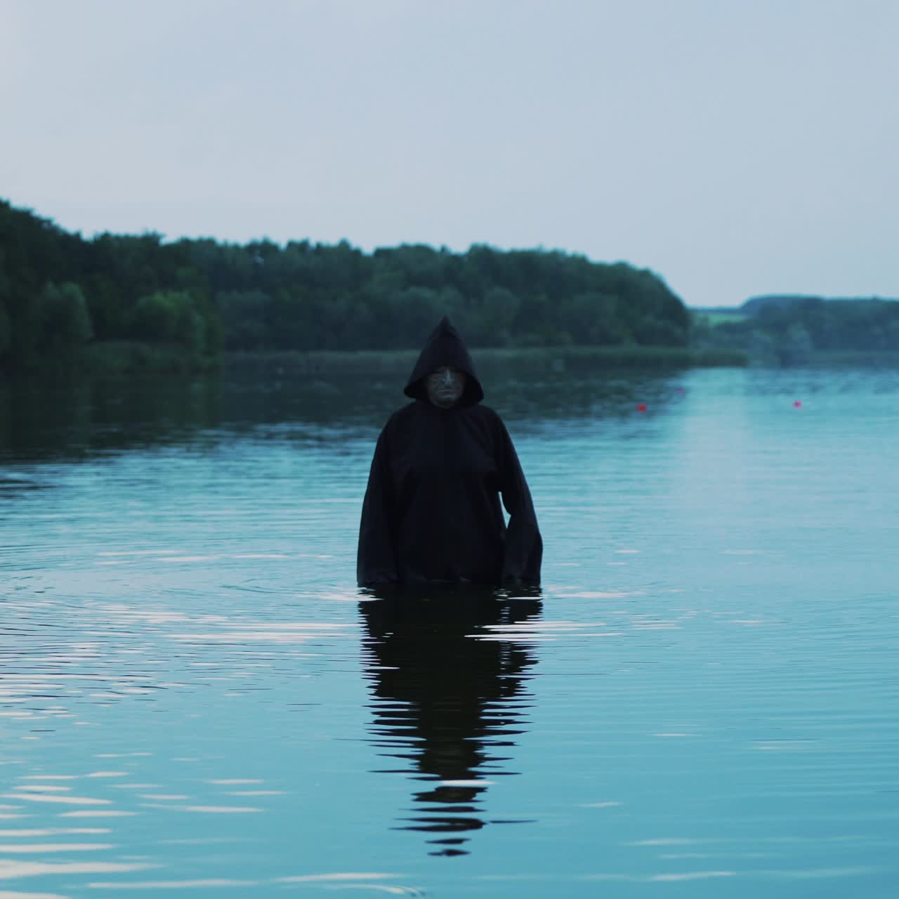 Ghost woman in the water outdoor. Scary figure in black mantle.