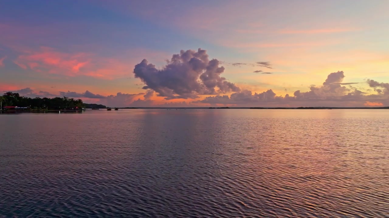 Veduta aerea di un tramonto rosa pastello sulla tranquilla laguna di Bacalar, Messico, con morbide nuvole luminose riflesse sull'ampia e immobile acqua turchese.