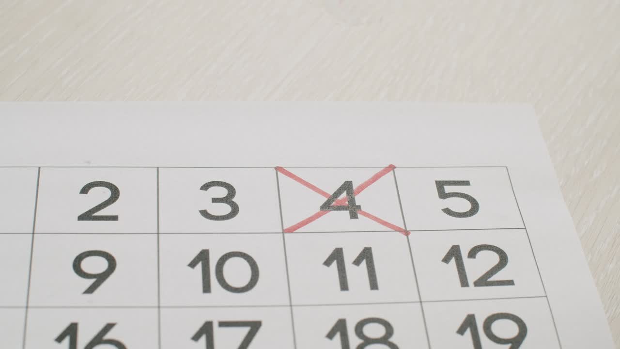la mano del hombre escribe el cuarto día en el calendario de papel usando un bolígrafo rojo.