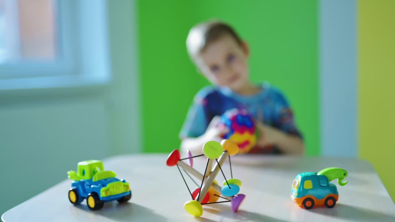 Educational games.Little boy playing alone with a toy. Bright toy cars and wooden plaything on the wooden table on blur boy background.