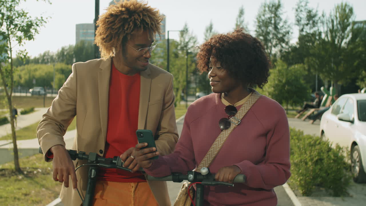 African American Friends Standing with E-Scooters in Park and Chatting