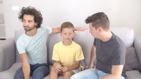 niño pensativo sentado en el sofá con sus dos padres