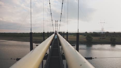 People-Walking-On-A-Hanging-Bridge-Across-The-River-On-A-Cloudy-Day