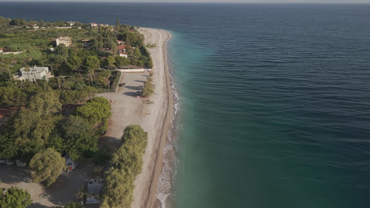 Inquadratura aerea frontale con drone sopra acque cristalline turchesi lungo la spiaggia con case costiere ad Akrata, Golfo di Corinto, Grecia, in una giornata di sole.