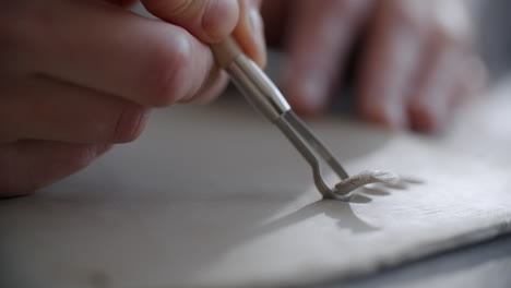 close-up of a potter using a tool to sculpt clay