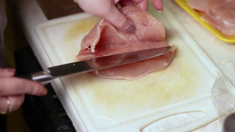 carefully cutting a piece of raw chicken breast through the middle in length