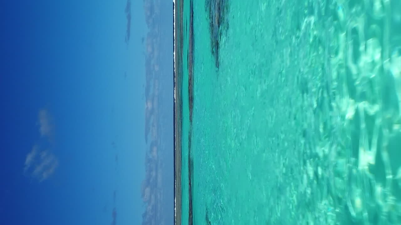 Low flyover above clear shallow water and coral reef near Mare Island in New Caledonia