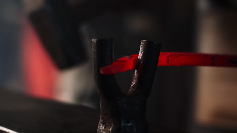 blacksmith bends an iron rod through a vice grip on an anvil in a metal workshop