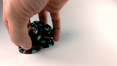 male hand shuffling black poker chips on a white table, still, isolated
