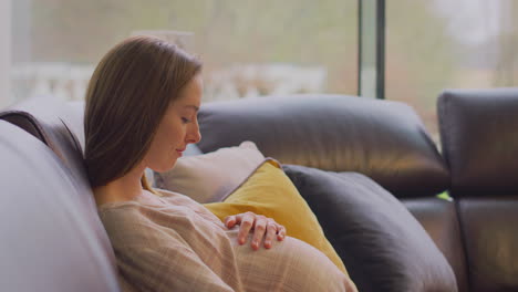 pregnant woman relaxing sitting on sofa at home watching tv