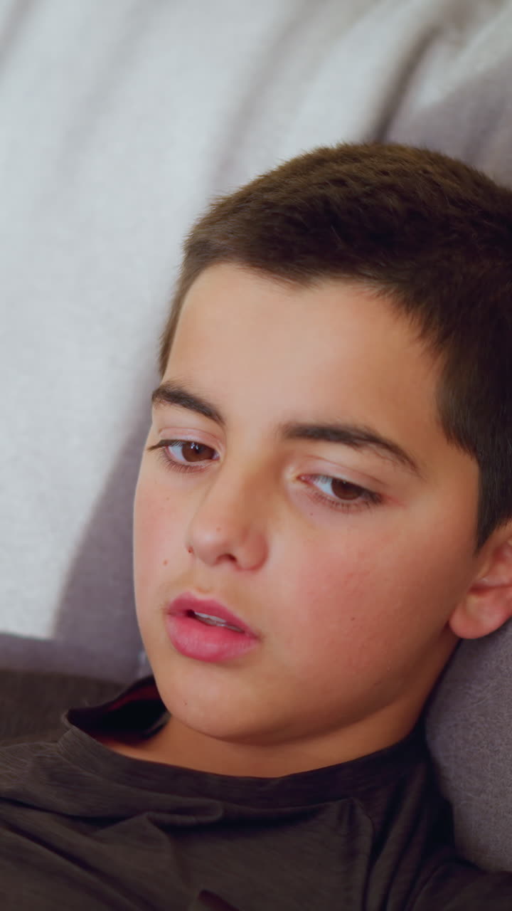 Friend removes thermometer from body of sick boy lying on couch in quiet indoor setting while checking reading showing empathy care and calm responsibility