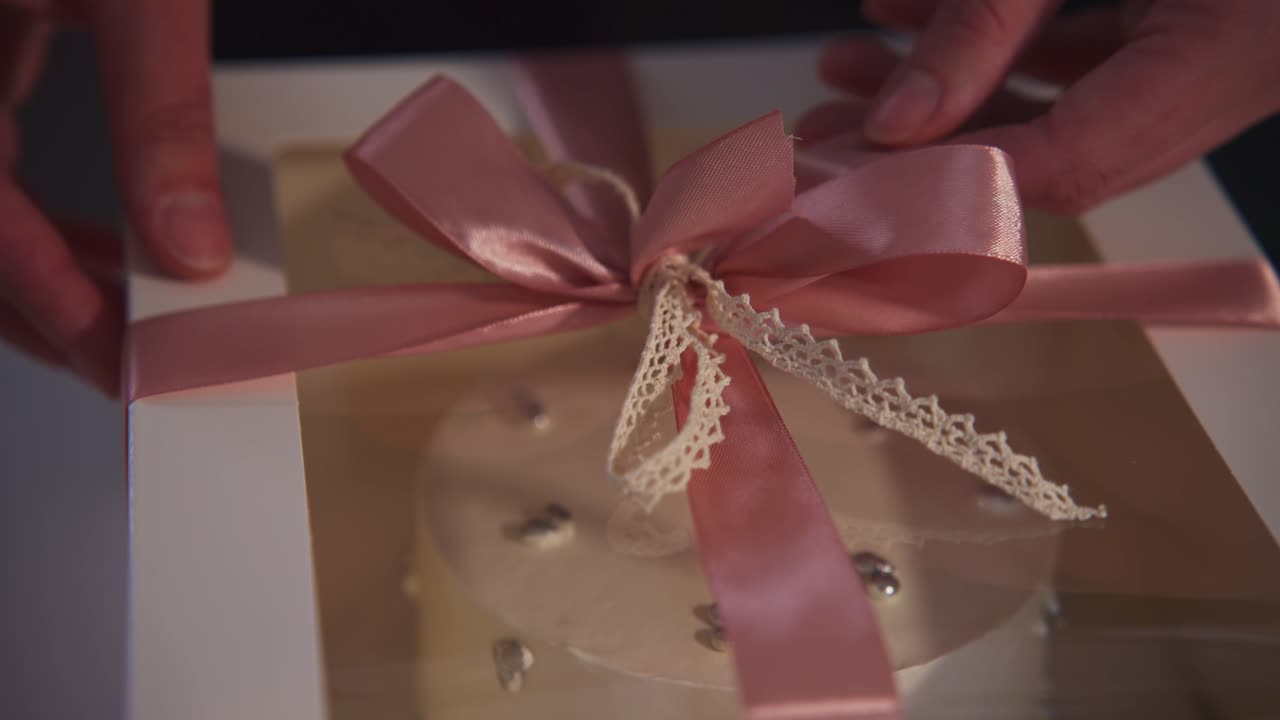 Close Up of Hands Adjusting a Pink Ribbon Bow on a Gift Box