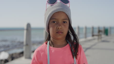 portrait young little mixed race girl looking serious kid smiling wearing beanie on sunny seaside beach slow motion