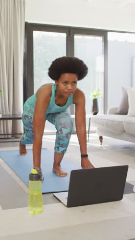 video vertical de una mujer afroamericana usando ropa deportiva y practicando yoga en casa