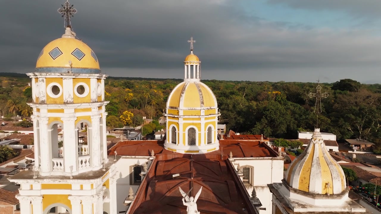 Vista aerea ascendente della facciata della Parroquia de San Miguel Arcángel nel centro storico di Comala, Colima, Messico, che rivela gli iconici campanili gemelli e la cupola centrale