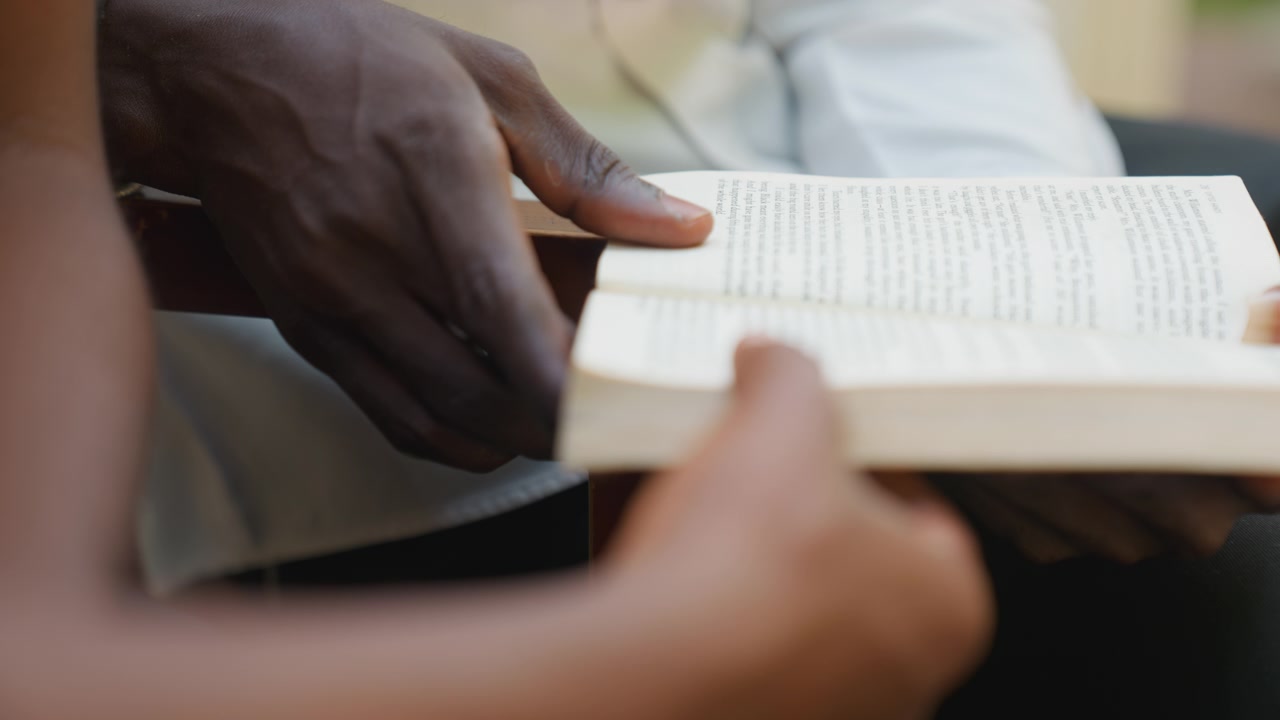 Closeup hands holding open book, romantic date couple sharing pages and poetry, gentle touch guiding page turn, soft natural light, warm tones, calm outdoor vibe, intimate connection and tenderness