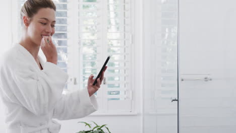 mujer biracial feliz cepillándose los dientes usando un teléfono inteligente en el baño, cámara lenta