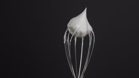 metal whisk with whipped egg whites, isolated on black background