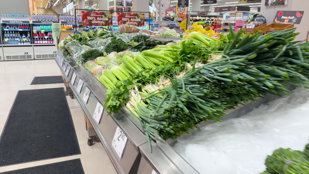 A handheld camera pans across fresh broccoli, cauliflower, and green onions in a bright supermarket