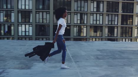 fashionable young woman on urban rooftop running and throwing her jacket