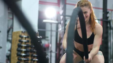 attractive young fit sportswoman working out in functional training gym doing exercise with battle ropes. slow motion