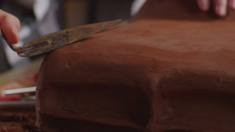 primer plano de las manos del diseñador automotriz usando una espátula para suavizar la superficie y crear detalles en la escultura de arcilla de automóvil en el estudio