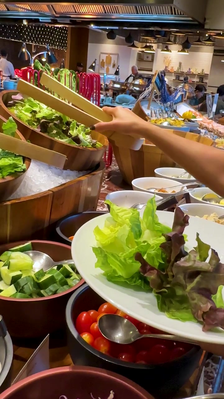 Una persona usa pinzas de madera para servirse lechuga fresca de un bufé en su plato.
