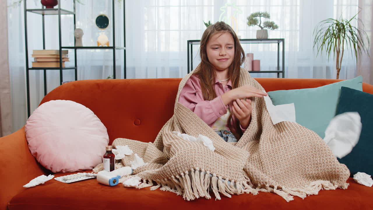 niña enferma niño que sufre de infección alérgica a la gripe fría envuelto en una manta se sienta en el sofá de la casa