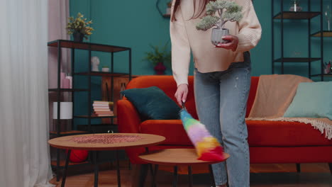 joven alegre limpiando el polvo de los muebles cuidando la higiene usando un polvo de colores en la sala de estar en casa
