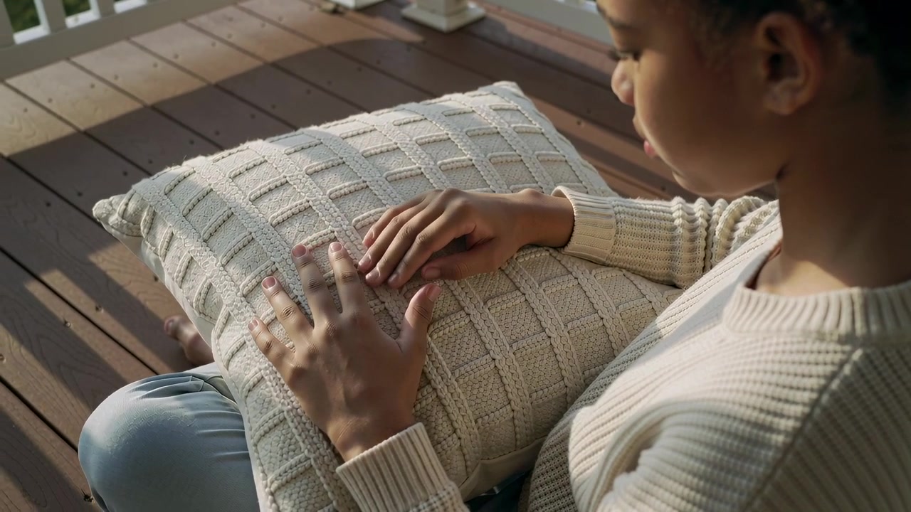 Tracing teen woman wearing knit sweater and blue pants exploring textured cushion on porch
