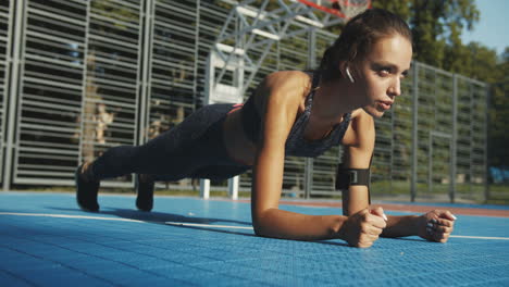 chica de fitness enfocada haciendo ejercicio de tabla en la cancha deportiva en un día de verano