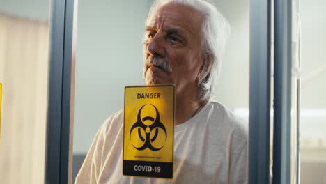 elderly man in isolation with covid-19 biohazard sign