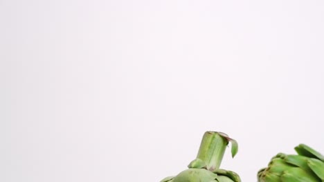 fresh green whole artichokes raining down on white backdrop and bouncing in slow motion